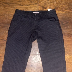 Svarta byxor från dondup storlek 12 - Snygga svarta byxor från dondup med diskret rutigt mönster. Byxorna har klassisk femficksdesign, raka ben och är tillverkade i bomullsmix. Insidan har coolt blommigt tyg vid fickorna som ger en unik touch. Perfekta för dig som gillar stilrena men ändå personliga plagg.