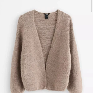 Beige stickad kofta från Lindex - Mysig beige stickad kofta från Lindex med avslappnad passform och lång ärm. Koftan är öppen framtill utan knappar och har en fluffig, mjuk känsla som passar perfekt till lager-på-lager. Enkel att styla till både jeans och kjol.