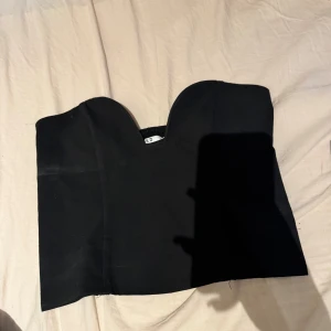 Svart tubtopp från NA-KD - Säljer en svart tubtopp från NA-KD i storlek 36. Toppen har en snygg sweetheart-urringning och är axelbandslös med elastisk baksida för extra komfort. Perfekt att styla med höga jeans eller kjol för en trendig look.(korsett topp)