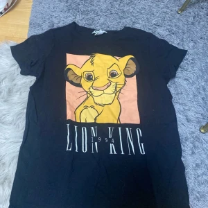 Svart Lion King t-shirt FB Sister S - Svart t-shirt från FB Sister med stort tryck av Simba från Lejonkungen och texten 'Lion King 1994' på framsidan. Klassisk rund hals och korta ärmar. Tillverkad i mjuk bomull, perfekt för dig som älskar Disney och vill ha en chill look.