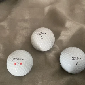 Titleist Pro V1 Golfbollar - Tre Titleist Pro V1 golfbollar i gott begagnat skick. Märkta med siffrorna 1, 2 och 6, en med små röda markeringar. Något smuts och mindre slitage synligt, men inga större skador. Perfekta för dig som vill ha premiumbollar till ett bra pris.
