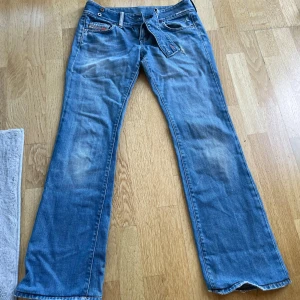 Blå bootcut jeans från Diesel - Snygga blå jeans från Diesel med bootcut passform och klassisk femficksdesign. Jeansen har slitna detaljer, låg midja och ett brett bälte i samma denimtyg. Perfekta för dig som gillar en avslappnad och trendig look.