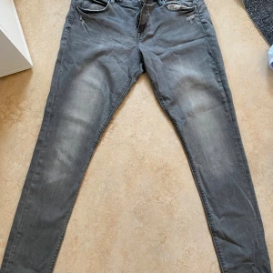 Grå low waist jeggings från &Denim - Snygga grå jeggings från &Denim med låg midja och dragkedja. Modellen är tight och har klassiska jeansfickor både fram och bak. Perfekta för dig som gillar en smal siluett och stretchigt material.