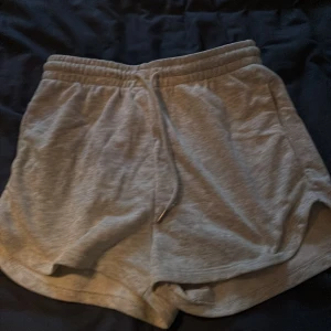 Grå mjuka shorts med snörning - Säljer ett par grå mjuka shorts med elastisk midja och snörning framtill. De har en avslappnad passform och är perfekta för chill dagar eller träning. Tillverkade i bomullsmix för extra komfort. Ingen lapp där bak finns inte kvar pga att den kliade på mig.