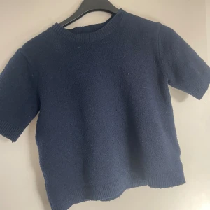 Marinblå stickad tröja från Kappahl - Mysig marinblå stickad tröja från Kappahl i storlek 158/164. Tröjan har korta ärmar, rund halsringning och ribbade muddar vid ärmslut och nederkant. Perfekt för lager-på-lager och chill dagar.