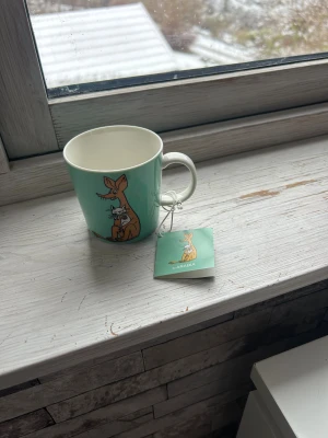 Sniff Muminmugg - Arabia Muminmugg med Sniff-motiv, i nyskick med originaletikett. Muggen är diskmaskin- och mikrovågssäker, perfekt för samlare eller Mumin-fans. Inga synliga defekter eller slitage, färgerna är klara och trycket är intakt. Aldrig använd 