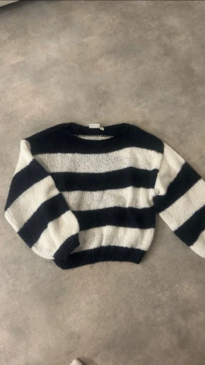 Randig stickad tröja i svart och vitt - Säljer en mysig stickad tröja med breda svarta och vita ränder. Tröjan har rund hals och långa ärmar med ribbade muddar vid ärmslut och nederkant. Perfekt för dig som gillar en chill och trendig look.