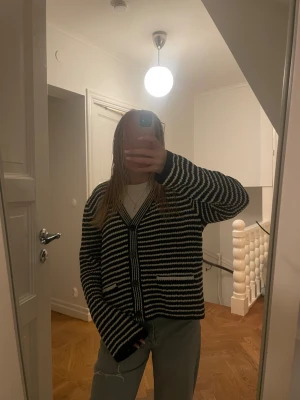 Svartvit randig kofta med knappar - Säljer en svartvit randig kofta med v-ringad hals och tre stora knappar framtill. Koftan har två små fickor och är stickad i mjukt material. Passar perfekt till jeans och har en loose fit som ger en chill vibe.