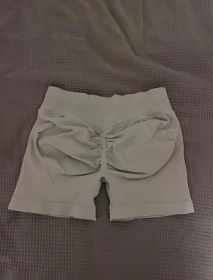 Grå seamless träningsshorts - Säljer ett par grå  träningsshorts med låg midja och scrunch-detalj bak för snygg form i rumpan. Materialet är stretchigt och mjukt, perfekt för gymmet. Dom är i storlek M men passar både mindre o större! Aldirg använda endast testade