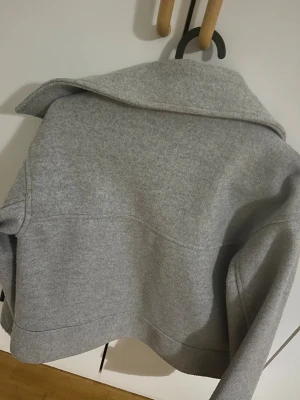 Grå kappa från Kappahl XS - Grå kappa från Kappahl i storlek XS. Jackan har  krage, stora framfickor och knäppning med knappar. Materialet är mjukt och känns som ull, perfekt för lager på lager.🩷🩷🩷Jätte fint skick köpt för 499 kr