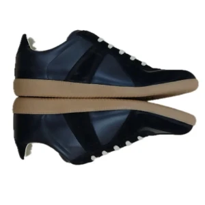 Maison Margiela svarta sneakers - Maison Margiela sneakers i svart skinn och mocka med beige snörning och gummisula i naturfärg. Klassisk rund tå och platt sula, med märkets ikoniska siffror på tungan. Snygg och stilren design som passar till streetwear och trendiga outfits.