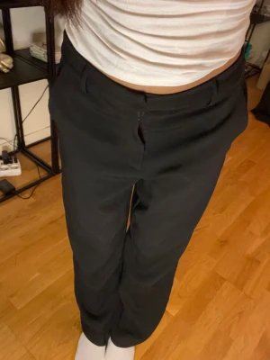 Svarta wide kostymbyxor - Snygga svarta kostymbyxor. Byxorna har klassiska fickor och bälteshällor. Materialet är mjukt och byxorna är i mycket bra skick. Varan säljs i befintlig skick och är lite större i storlek. 