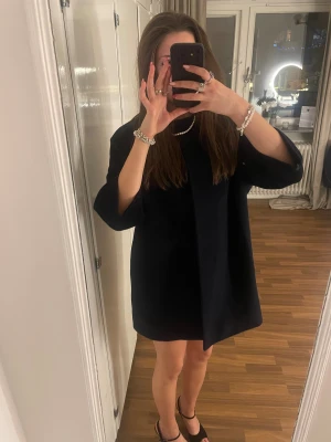 Mörkblå kappa med 3 kvarts ärm - Säljer en stilren mörklblå kappa med rak passform och tre kvarts ärm från Cos i storlek S. Kappan knappar är dolda. Den passar med jeans men på bilden bär jag kjol under. Knapparna är lite luddiga. Hör av dig vid frågor.🩷☺️