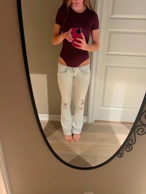 Ljusblå bootcut jeans med slitningar - Säljer ett par ljusblå jeans med bootcut fit och låg midja. Byxorna har slitna detaljer på knäna och klassiska fem fickor. Jeansen är tillverkade i denim och har en enkel design med dragkedja och knapp framtill. De mest drömmiga jeansen som är helt superrrr❣️❣️❣️