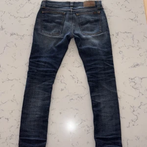 Blå slim fit jeans Nudie Jeans - Säljer ett par navy blåa Nudie Jeans. INGA DEFEKTER förutom använd har en tvättad look  skick är ganska bra 8/10 inga skador men täcken på andvänt är i storlek 26W men passar 28 mer.  28W 32L priset kan diskuteras och NYPRIS är 2000kr