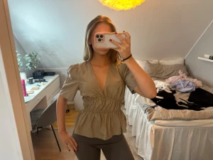 Beige omlottblus från Modström - Säljer en beige blus från Modström i storlek XS. Blusen har korta puffärmar, djup v-ringning och omlottdetalj med smock i midjan som ger en snygg siluett. Materialet är mjukt och lätt, perfekt för dig som gillar stilrena och trendiga plagg.