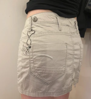 Beige kortkjol från G-Star - Säljer en beige kortkjol från G-Star med detaljer på fickor, bälteshällor och knappstängning fram. Kjolen är tillverkad i bomull och har en urban streetstil med snygga sömmar och logotyp på bakfickan. Säljs för att den inte kommer till användning💕