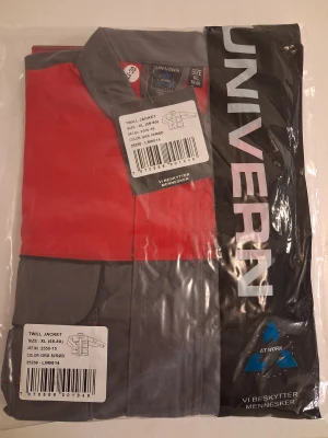 Grå och röd twilljacka från Univern XL - Säljer en grå och röd twilljacka från Univern i storlek XL. Jackan har klassisk krage, långa ärmar och flera praktiska fickor framtill. Materialet är slitstark bomull och polyester, perfekt för dig som vill ha en cool och funktionell look.