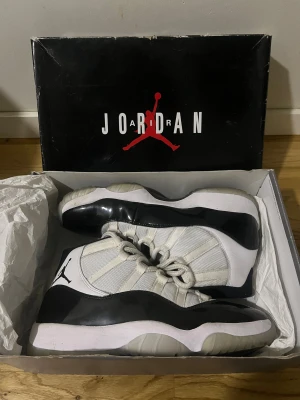 Nike Air Jordan 11 Retro Concord - Nike Air Jordan 11 Retro Concord i storlek 42.5. Skorna har en clean vit och svart färg med mesh och lackdetaljer, samt klassisk snörning och rund tå. Ikonisk Jumpman-logga på sidan och genomskinlig sula. Perfekt för dig som vill ha en riktigt fet sneaker med retrovibe.helt äkta 