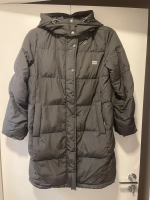 Levis vinterjacka  - En tjock och varm vinterjacka, går ungefär till mitten på låren. Fin använd, så inga synliga tecken på användning. Dragkedjsfickor, samt dragkedja för att stänga jackan samt knappar där. Luvan är avtagbar med dragkedja.