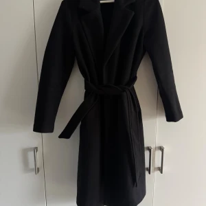 Svart kappa från Vero Moda med bälte - Stilren svart kappa från Vero Moda med klassisk krage och knytskärp i midjan. 