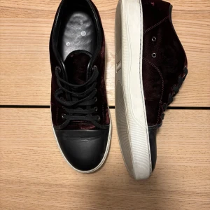 Vinröda sneakers med svart tå - Snygga sneakers i vinröd sammet med svart tå och snörning. Skorna har en vit platt sula och svarta detaljer runt öppningen. Perfekta för dig som vill ha en unik och cool stil med lite lyxig känsla.