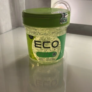 Eco Style Olive Oil hårgel - Eco Style Olive Oil hårgel i en rund plastburk med grön lock. Gelen är transparent med en svagt gul ton och har en lätt, geléaktig konsistens. Perfekt för att styla och ge glans till håret. Innehåller olivolja som återfuktar och ger maximal stadga.