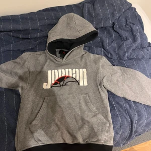 Grå Jordan hoodie med tryck - Säljer en grå hoodie från Jordan med stor logga och basketboll-tryck i vitt, svart och rött på både fram- och baksidan. Tröjan har huva, känguruficka och svarta detaljer inuti luvan. Perfekt för dig som gillar sportig streetstyle. Jag köpa det i American nike outlet 70€