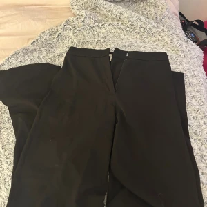 Svarta kostymbyxor från H&M, strl 34 - Snygga svarta kostymbyxor från H&M i storlek 34. Byxorna har en rak passform med midwaist och diskret dragkedja i sidan. Perfekta för en clean och stilren look. Materialet är mjukt och har en lätt stretch för extra komfort.