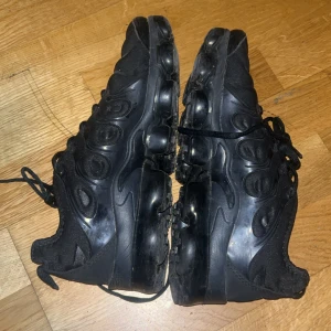 Svarta Nike Air Vapormax sneakers - Säljer ett par helsvarta Nike Air Vapormax sneakers med reflekterande detaljer på ovandelen. Skorna har en unik bubblig sula och snörning framtill. Ovandelen är i syntet och textil, med diskret Nike-logga och 'Vm Air' märke på hälen.