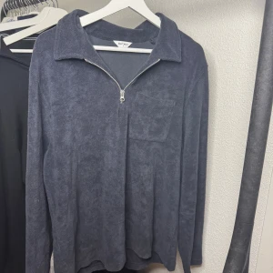 Mörkgrå frottétröja från East West - Mjuk och skön långärmad tröja i mörkgrå frotté från East West. Tröjan har en halv dragkedja framtill, klassisk krage och en bröstficka. Perfekt för en avslappnad och chill stil.