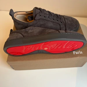Christian Louboutin grå mockasneakers - Snygga sneakers från Christian Louboutin i mörkgrå mocka med klassisk röd sula och rund tå. Skorna har snörning och en stilren design som sticker ut med den ikoniska röda undersidan. Perfekta för dig som vill ha något exklusivt och trendigt. Hör av er vid någon fråga eller vill ha en extra bild! Priset kan diskuteras vid snabb affär!✅