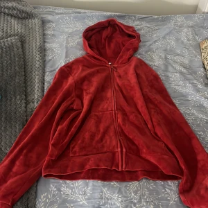Röd velour hoodie med dragkedja - Mjuk och skön röd hoodie i velour med hel dragkedja framtill och huva. Tröjan har långa ärmar och en klassisk känguruficka. Perfekt för chill dagar eller när du vill ha en cozy vibe. Snyggt enkel design som funkar till jeans eller mjukisbyxor.