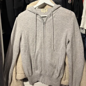 Ljusgrå zip up i kashmir från Soft Goat - Mysig ljusgrå hoodie från Soft Goat i mjuk kashmir. Tröjan har dragkedja framtill, snörning i huvan och ribbade muddar. Perfekt för dig som vill ha en stilren och skön look med premiumkänsla.