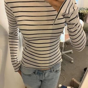 Vit och blå randig båtringad tajt tröja  - Vit långärmad tröja med mörkblå horisontella ränder. Tröjan har en smickrande tight passform och är tillverkad i mjuk bomull. Fin båtringning som går ända ut till axlarna, går därför också att ha som en off shoulder topp. Liten slits i ärmarna som syns på bild 4