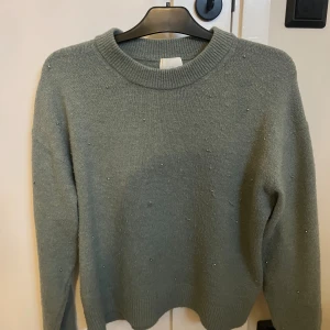 Grön stickad tröja med pärlor - Snygg grön stickad tröja från H&M med rund hals och långa ärmar. Tröjan har små pärlor som detalj över hela framsidan.