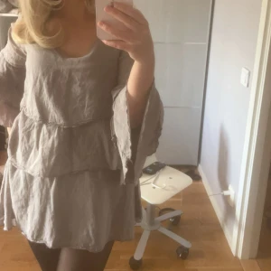 Beige volangklänning i linne - Superfin beige kortklänning med volanger och vida ärmar. Klänningen har v-ringning och är tillverkad i ett svalt linnematerial. Perfekt för dig som gillar en bohemisk och avslappnad stil. Sitter löst och har en flowy känsla.