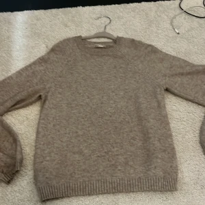 Beige stickad tröja från ONLY - Mysig beige stickad tröja från ONLY med rund hals och ribbade muddar vid ärmslut och nederkant. Perfekt för dig som gillar enkel och clean stil. Passar dig som vill ha en basic tröja med lite loose fit och långärmad design.