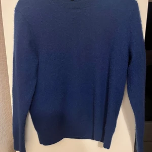 Blå kashmirtröja från Uniqlo - Mjuk och lyxig blå kashmirtröja från Uniqlo i storlek S. Tröjan har rund hals, lång ärm och en enkel, klassisk design utan mönster eller detaljer. Perfekt för dig som gillar stilrena och bekväma plagg med premiumkänsla.