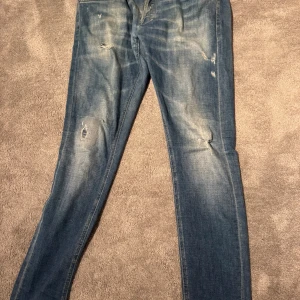 Blå skinny jeans från George, stl 32 - Snygga blå skinny jeans från George i storlek 32. Jeansen har slitna detaljer och lätt tvättad look, med klassiska fem fickor och skinny fit. Perfekt för dig som gillar en smal siluett och lite ruffigare stil.