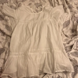 Vit somrig blus med volang - Gina tricot, strl  158/164🤍Luftig vit blus med volangdetaljer och fina spetsinslag. Klänningen har korta ärmar och en lös passform, perfekt för varma dagar. Tillverkad i ett lätt och mjukt material som ger en avslappnad och bohemisk känsla.🤍