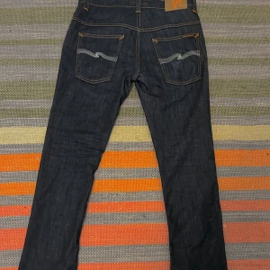 Nudie Jeans Thin Finn mörkblå jeans - Riktigt feta mörkblå jeans från Nudie Jeans, modell Thin Finn. Klassisk femficksdesign med kontrastsömmar och snygga broderade bakfickor. Storlek W31 L32. Skick: Nyskick