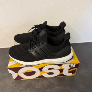 Adidas Ultraboost svarta sneakers - Svarta Adidas Ultraboost sneakers med stickad ovandel och klassiska tre ränder på sidan. Skorna har en vit, responsiv Boost-sula och svart yttersula med mönstrad greppyta. Perfekt för dig som gillar stilrena och sportiga sneakers med skön komfort.
