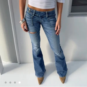 Blå bootcut jeans med låg midja - Snygga blå jeans från Gina med bootcut och låg midja. Jeansen har slitningar på låret, två framfickor och dubbla knappar i midjan. Perfekta för en trendig och avslappnad look. Strl M