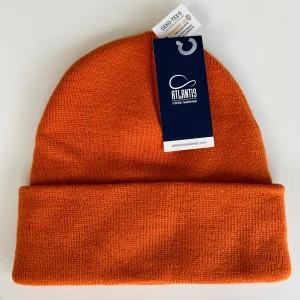 Orange stickad mössa från Atlantis - Snygg orange beanie från Atlantis, tillverkad i mjukt stickat material. Mössan har klassisk form med uppvikt kant och är certifierad enligt OEKO-TEX Standard 100. 