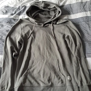 Grå hoodie från Jack & Jones - Snygg grå hoodie från Jack & Jones Essentials med klassisk känguruficka och dragsko i huvan. Tröjan är i mjuk bomull och har ribbade muddar vid ärmslut och nederkant. Perfekt för chill dagar eller när du vill ha en enkel och stilren look.