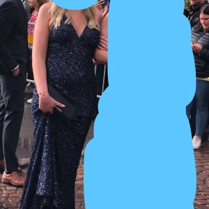 Balklänning dressroom - Säljer en marinblå långklänning med glittriga paljetter och v-ringad hals. Klänningen har smala axelband som korsas i ryggen och en öppen rygg från dressromm. Nypris 5000 kr jag säljer för 2500 eftersom det lossnat en del paljetter på släpet men inget iallafall jag tänker på