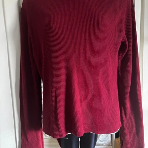 Vinröd ribbad tröja från Rodebjer - Vinröd långärmad tröja från Rodebjer med ribbad struktur. Tröjan har en rak passform och är tillverkad i en mjuk blandning av rayon och bomull. Perfekt för dig som gillar stilrena och bekväma plagg med en modern touch.