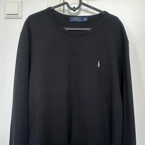 Svart långärmad tröja Polo Ralph Lauren - Svart långärmad tröja från Polo Ralph Lauren med klassisk rund halsringning och broderad logga på bröstet. Tillverkad i mjuk bomull som känns skön mot huden. Perfekt för en clean och stilren look.