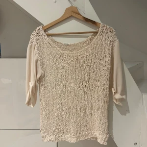 Beige American Vintage tröja - Säljer en beige stickad tröja från American Vintage med snyggt grovstickat framstycke och mjuka, enfärgade ärmar i trekvartsmodell. Tröjan har avslappnad passform och rund halsringning, perfekt för lager-på-lager-stil.